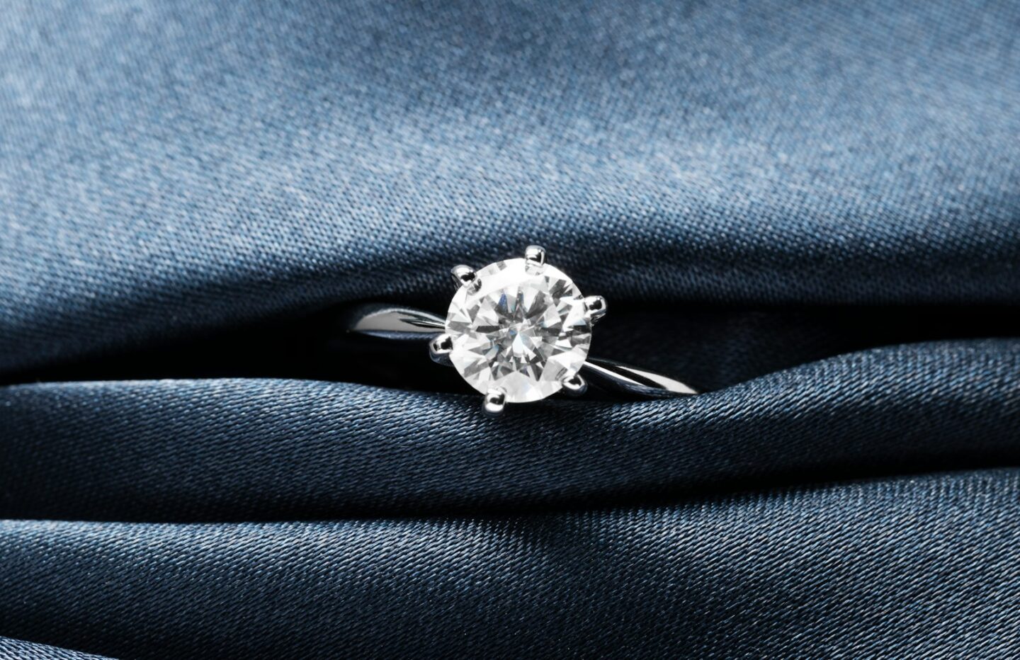 A close up of a diamond ring on a blue cloth